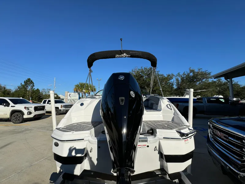 Slide: The Image of 2025 NauticStar 243 DC Deck boat with outboard motor, parked outdoors. - 8
