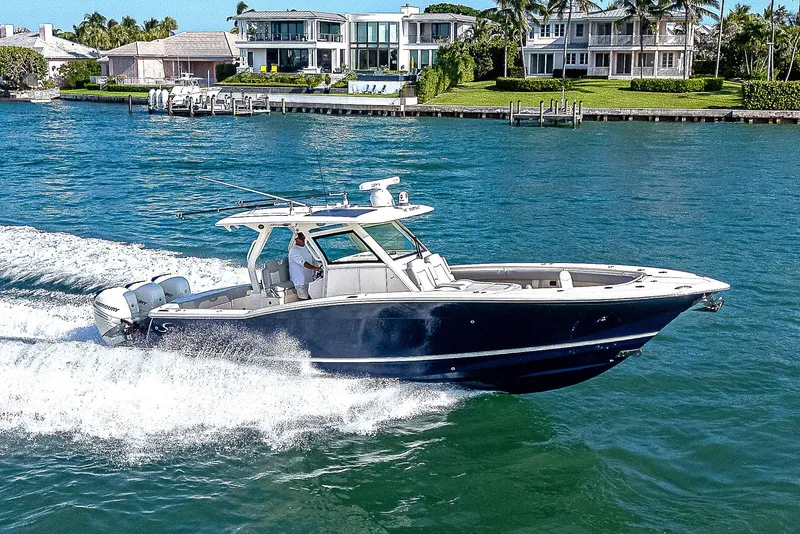Slide: The Image of 2023 Scout LXF boat cruising on clear blue water near luxury waterfront homes. - 38
