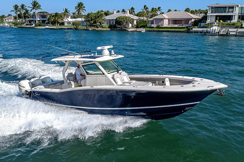 Slide: The Image of 2023 Scout LXF boat cruising on a sunny waterfront with luxury homes. - 45