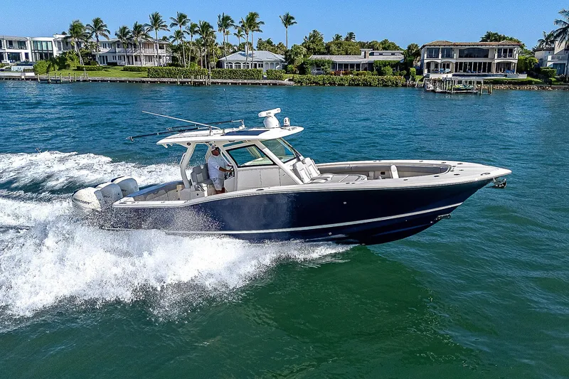 Slide: The Image of 2023 Scout LXF boat cruising on a sunny day near waterfront homes. - 46