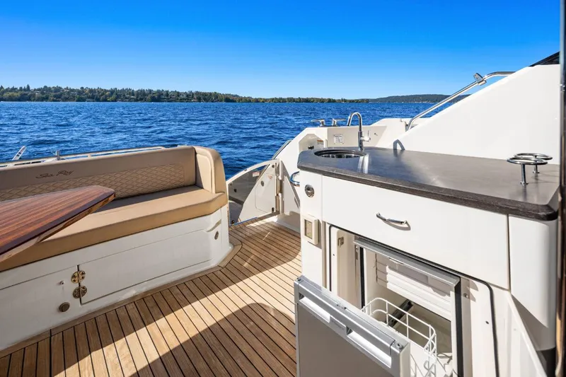 Slide: The Image of 2017 Sea Ray L590 Sport yacht deck with seating and kitchenette, overlooking serene blue waters. - 39
