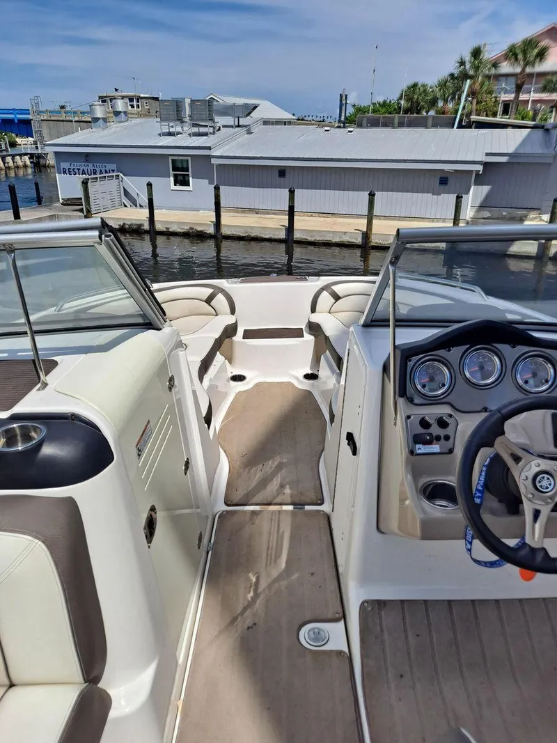 Slide: The Image of 2013 Yamaha Boats 242 Limited S interior with dashboard and seating, docked by waterfront buildings. - 23