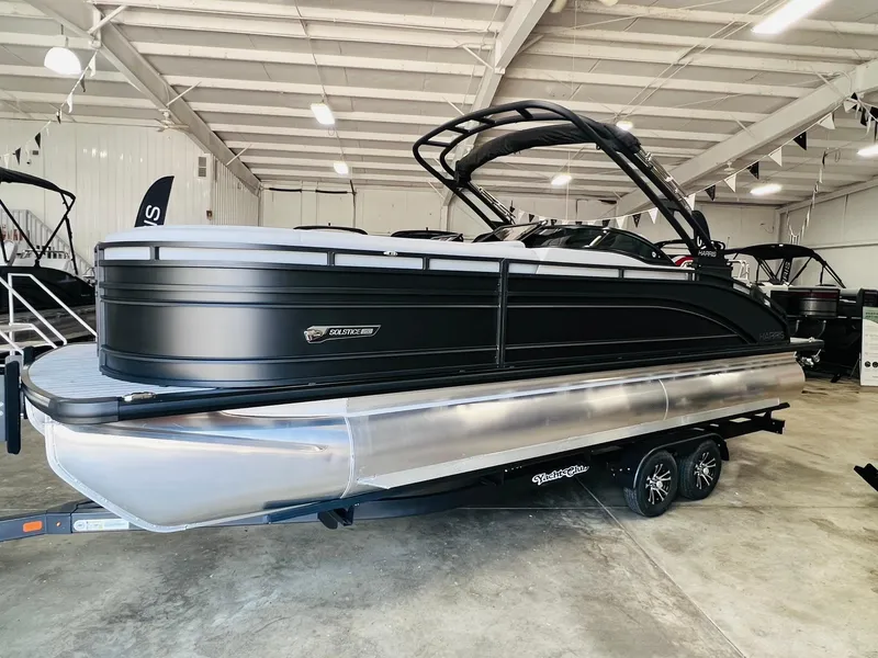 Slide: The Image of 2025 Harris Solstice DC 250 pontoon boat in showroom, sleek black design on trailer. - 2