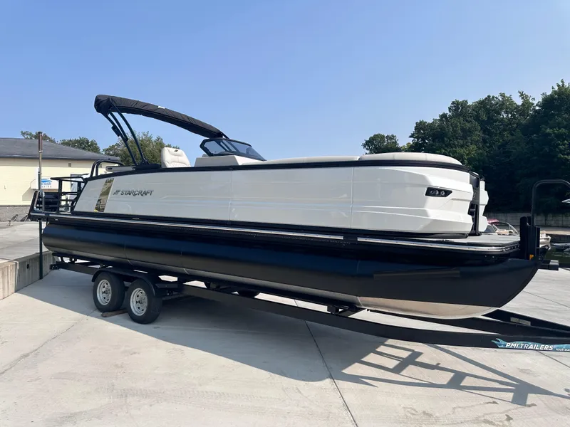 The Image of 2025 Starcraft RX 25 DL DC pontoon boat on trailer, parked outdoors. - 0