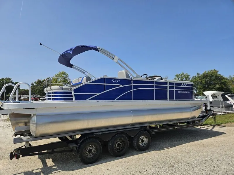 Slide: The Image of 2025 Bennington 22 SXSB pontoon boat on trailer, blue and silver design, sunny day. - 10
