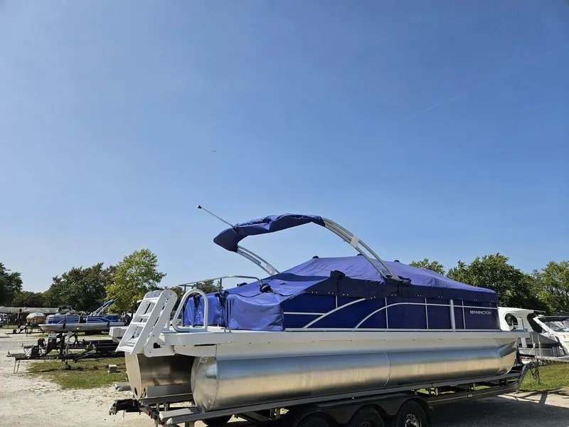 Slide: The Image of 2025 Bennington 22 SXSB pontoon boat with blue cover, parked on a trailer. - 5
