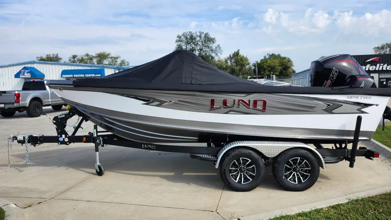 Slide: The Image of 2025 Lund 1875 Tyee boat on trailer, covered, parked outdoors. - 2