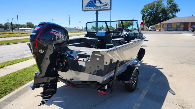 Slide: The Image of 2025 Lund 1775 Impact XS Sport boat with powerful outboard motor in a parking lot. - 2