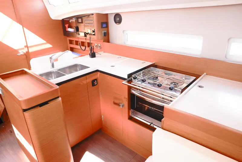 Slide: The Image of Modern kitchen in 2022 Jeanneau Sun Odyssey 410 yacht, featuring stove, sink, and wooden cabinetry. - 4