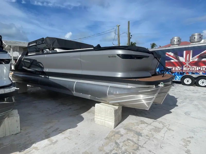 Slide: The Image of 2025 Manitou 26 Explore Switchback pontoon boat on concrete blocks, outdoor setting. - 4