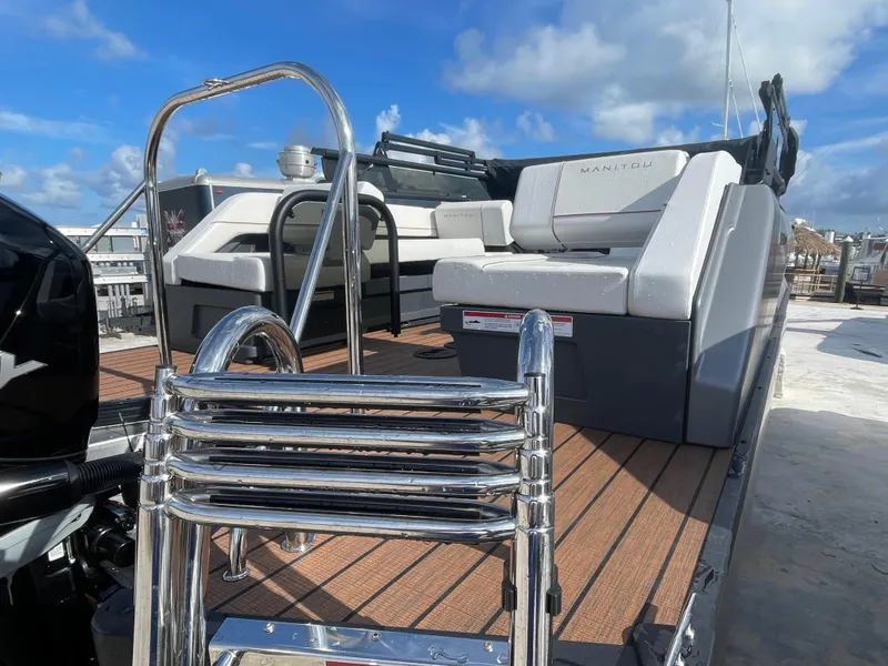 Slide: The Image of 2025 Manitou 26 Explore Switchback boat with seating and ladder under a clear blue sky. - 6