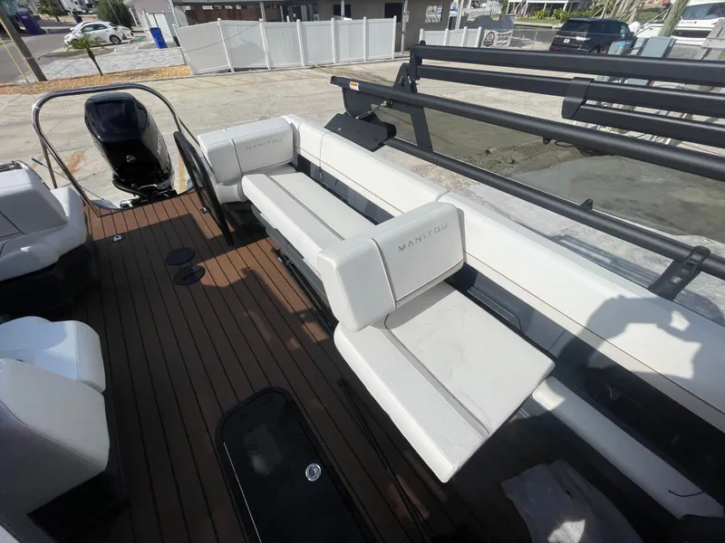 Slide: The Image of 2025 Manitou 26 Explore Switchback boat interior with white seating and wooden deck. - 7
