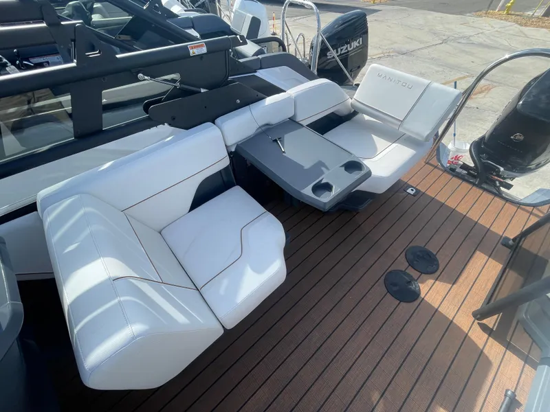 Slide: The Image of 2025 Manitou 26 Explore Switchback boat interior with white seating and wooden deck. - 9