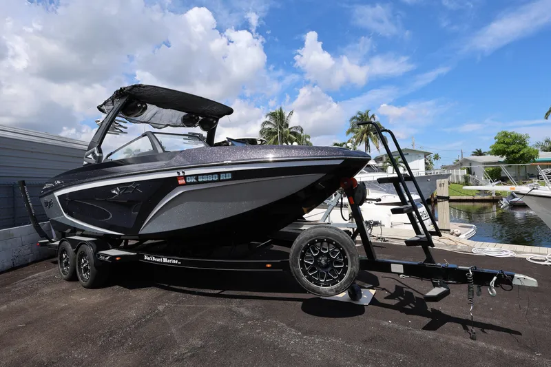 Slide: The Image of 2021 Tigé 23ZX boat on trailer, parked near waterfront under blue sky. - 1