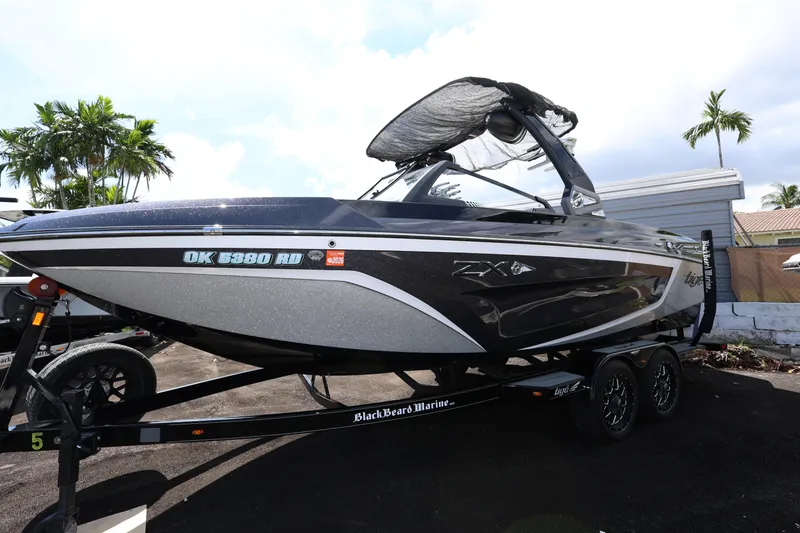 Slide: The Image of 2021 Tigé 23ZX boat on trailer, parked outdoors, with palm trees in background. - 3