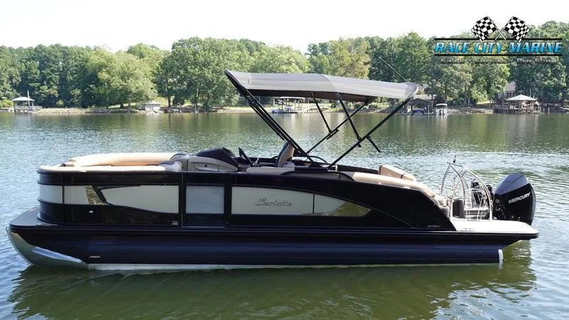 Slide: The Image of 2025 Barletta L23U pontoon boat on a serene lake with lush green trees. - 2