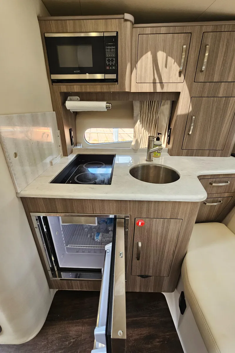 Slide: The Image of 2022 Regal 33 XO boat kitchen with microwave, sink, and fridge. - 26