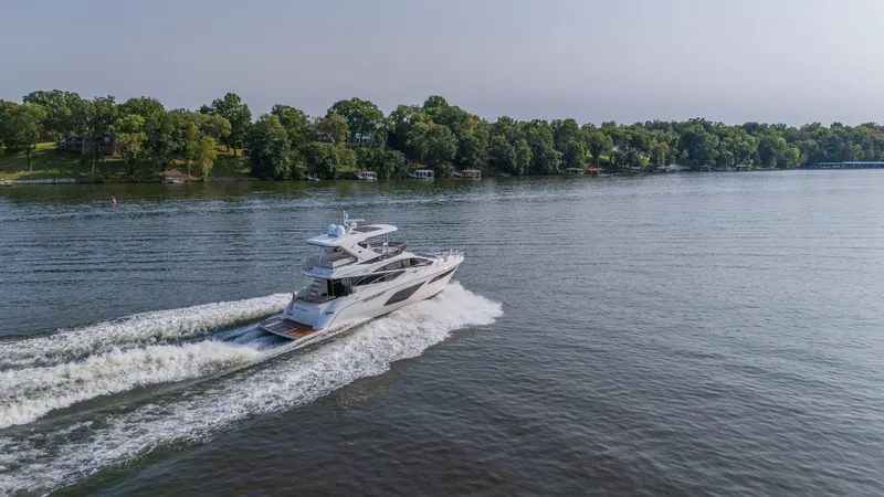 Slide: The Image of 2018 Sea Ray L550 Fly yacht cruising on a serene lake with lush green shoreline. - 6