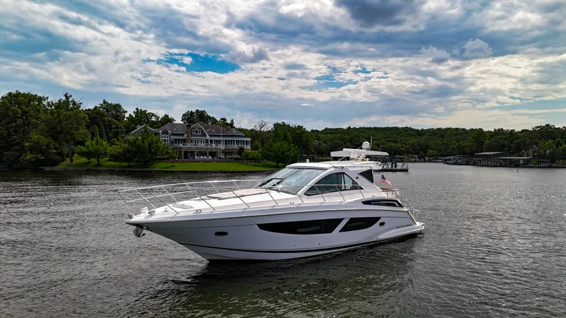 The Image of 2017 Regal 53 Sport Coupe yacht cruising on a scenic lake with lush greenery. - 0
