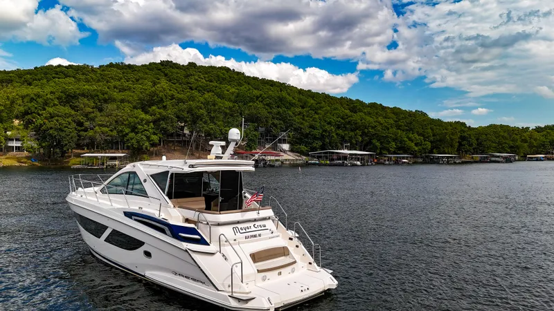 Slide: The Image of 2017 Regal 53 Sport Coupe yacht on a serene lake with lush green shoreline. - 4