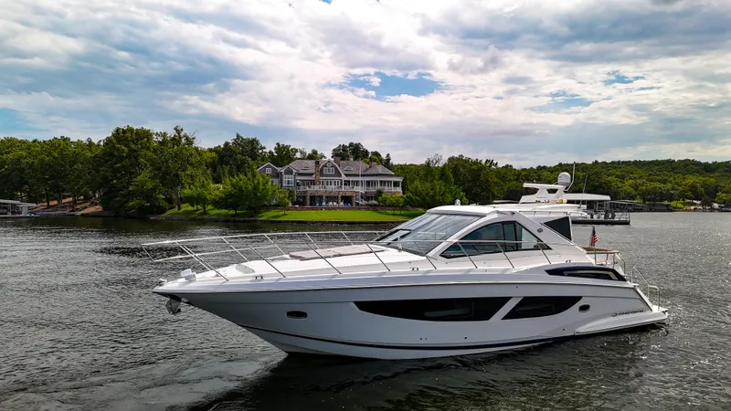 Slide: The Image of 2017 Regal 53 Sport Coupe yacht cruising on a scenic lake with lush greenery. - 7