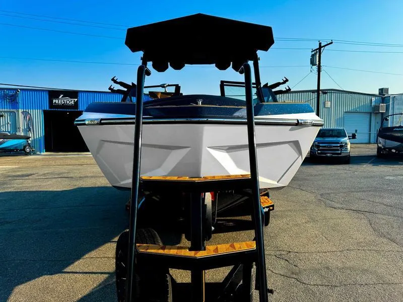 Slide: The Image of 2025 Tigé ULTRE 23ZX boat on trailer, parked outdoors near industrial buildings. - 5