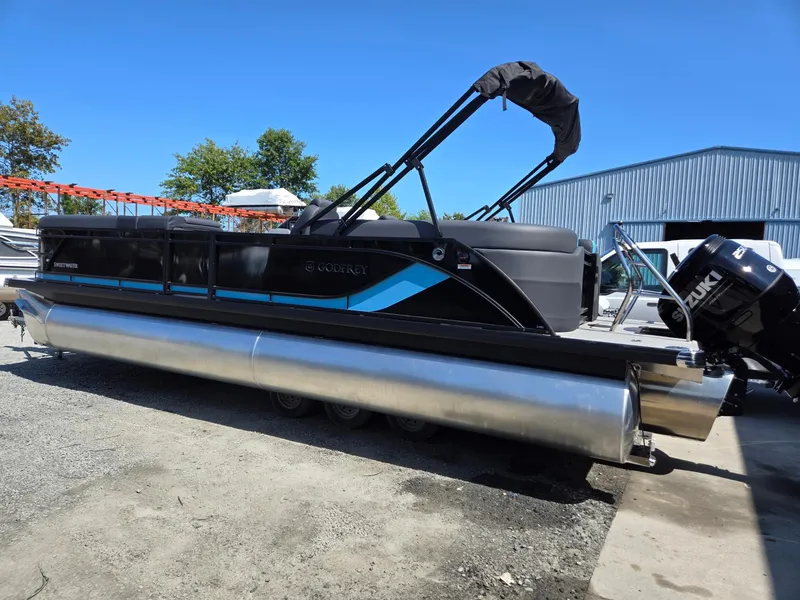 Slide: The Image of 2025 Godfrey Sweetwater 2486 SB pontoon boat with Suzuki outboard motor, parked outdoors. - 3
