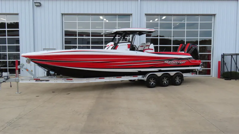 The Image of 2025 Sunsation 32 CCX boat with red and white design on a trailer outside a building. - 0