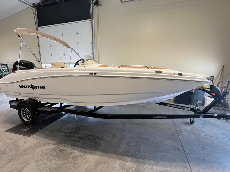 The Image of 2025 NauticStar 203 SC Deck boat on trailer in indoor storage. - 0
