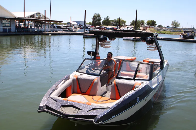 Slide: The Image of 2017 Tigé RZX3 boat on water, featuring orange and gray interior, dock in background. - 15