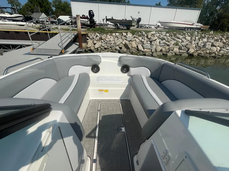 Slide: The Image of 2021 NauticStar 223 DC Deck boat interior with gray seating, docked by rocky shore. - 12