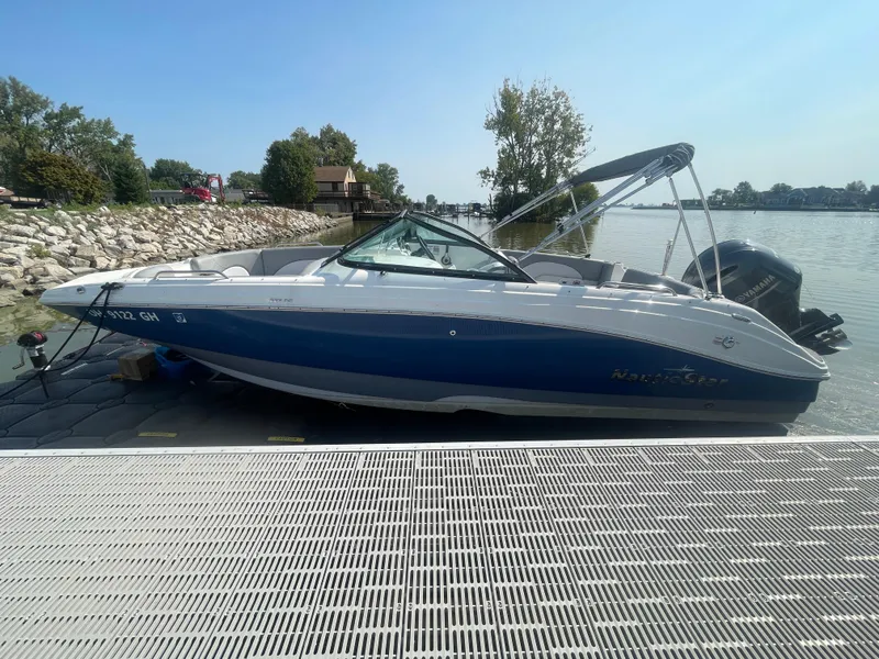 Slide: The Image of 2021 NauticStar 223 DC Deck boat docked by a serene lakeside. - 20