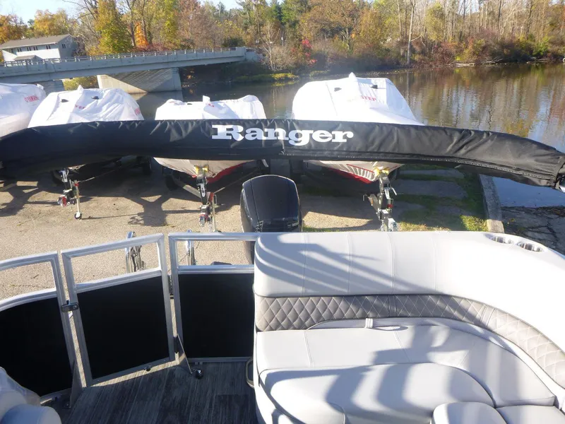 Slide: The Image of 2024 Ranger Reata 223C pontoon boat with covered motor, docked near a serene lake. - 7