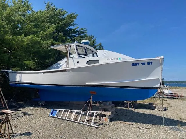 The Image of Crowley-Beal 28 boat, 1996 model, white hull, blue bottom, on land with trees and ocean background. - 0