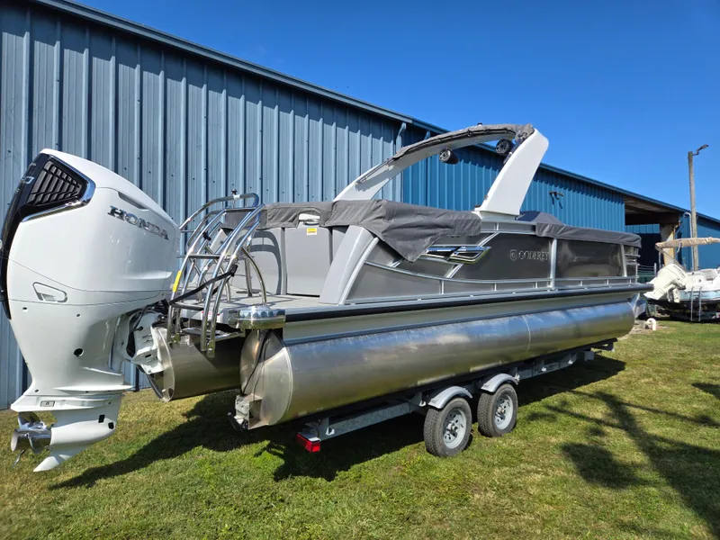Slide: The Image of 2025 Godfrey AquaPatio 255 ULC pontoon boat on trailer, parked near blue building. - 2
