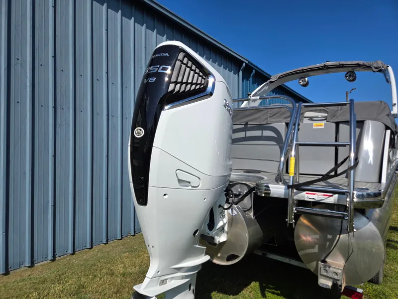 Slide: The Image of 2025 Godfrey AquaPatio 255 ULC boat with powerful outboard motor, parked beside a blue building. - 3