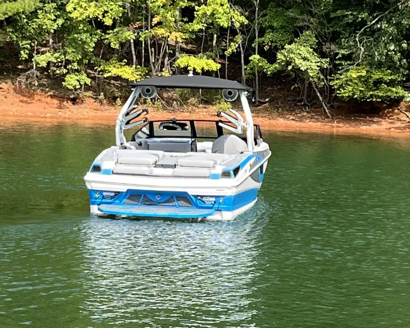Slide: The Image of 2025 Centurion Fe23 boat on a serene lake with lush green trees. - 2