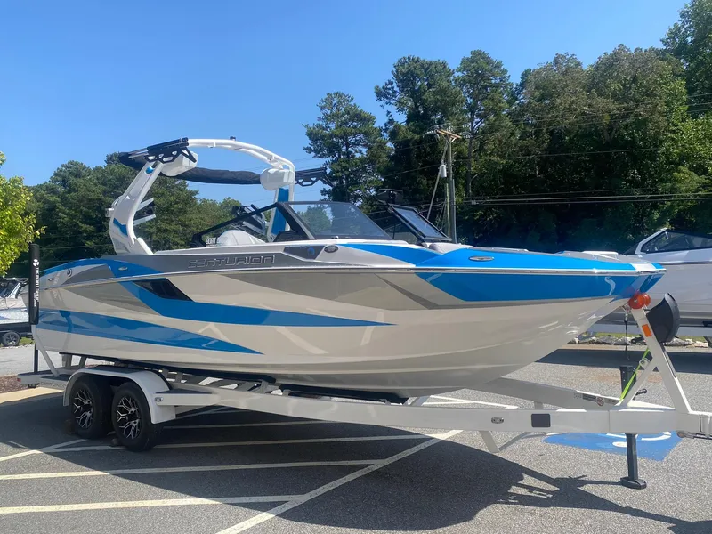 Slide: The Image of 2025 Centurion Fe23 boat with blue and white design on a trailer in a parking lot. - 6