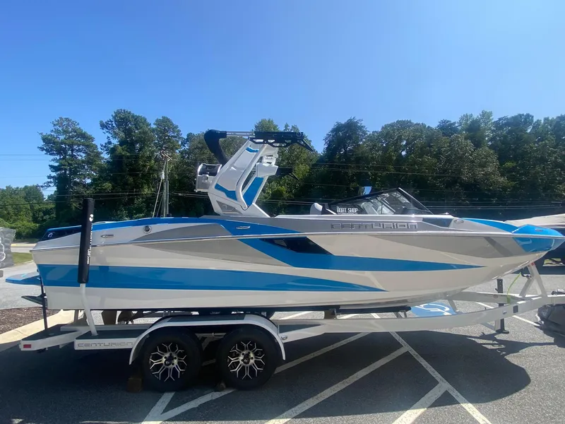 Slide: The Image of 2025 Centurion Fe23 boat on trailer, blue and white design, parked outdoors. - 7