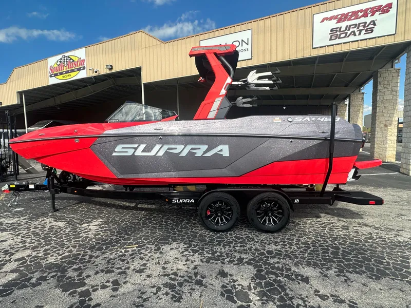 Slide: The Image of 2025 Supra SA 450 boat in red and gray, parked outside dealership. - 2