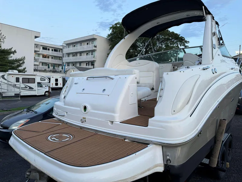 Slide: The Image of 2006 Sea Ray 280 Sundancer boat with spacious deck, parked in urban setting. - 12
