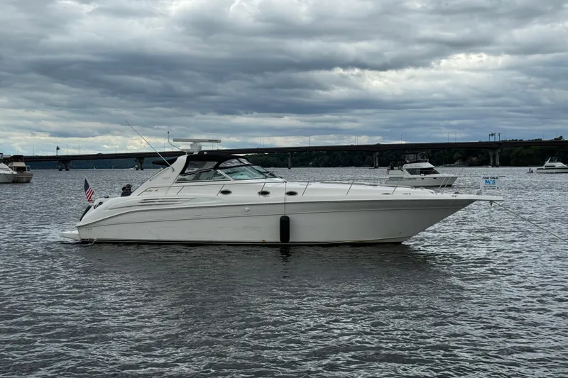 The Image of 1997 Sea Ray 450 Sundancer yacht anchored on a calm lake under a cloudy sky. - 0
