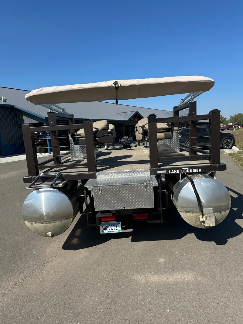 Slide: The Image of 2021 Lake Lounger 13FISH4E pontoon boat with canopy, parked on pavement under clear blue sky. - 3