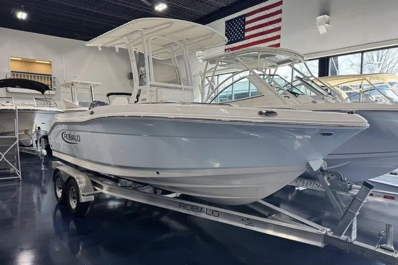 The Image of 2025 Robalo R 200 CC boat on trailer in showroom with American flag. - 2
