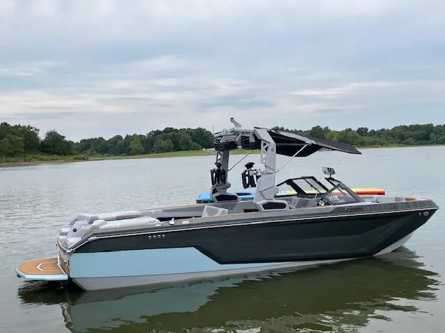 Slide: The Image of 2024 Nautique GS24 boat on a calm lake with lush green shoreline. - 1