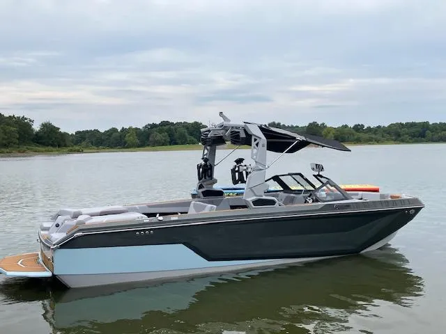 Slide: The Image of 2024 Nautique GS24 boat on a calm lake with lush green shoreline. - 16