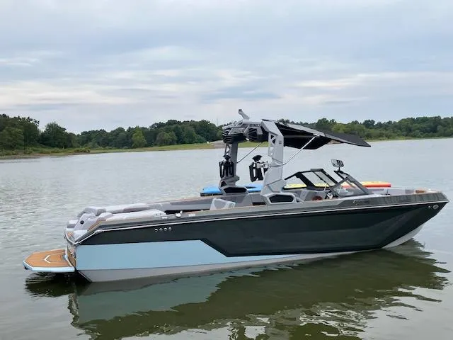 Slide: The Image of 2024 Nautique GS24 boat on a calm lake with lush green shoreline. - 17