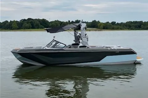 Slide: The Image of 2024 Nautique GS24 boat on a calm lake with lush green shoreline. - 2