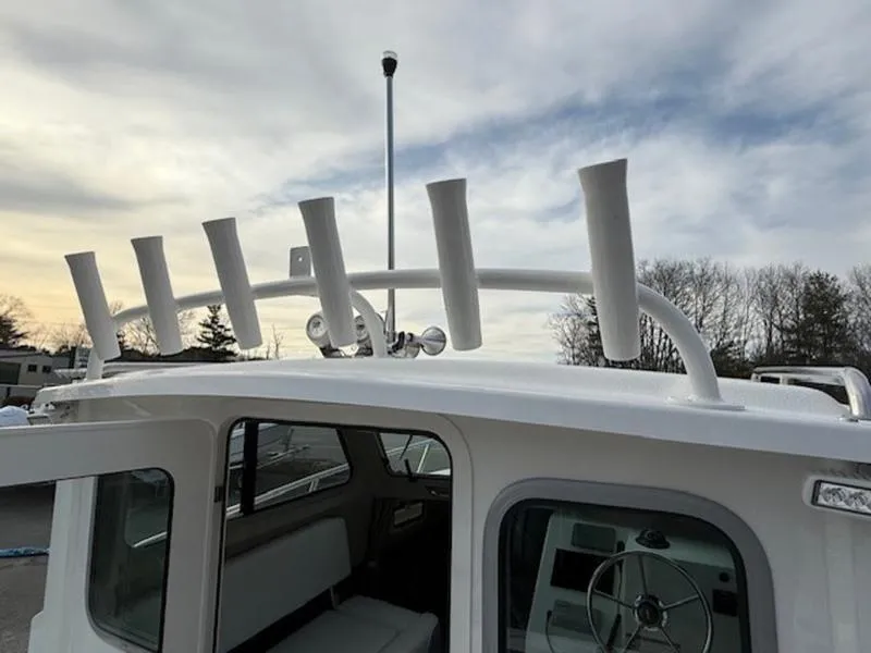 Slide: The Image of 2025 Parker 2120 Sport Cabin boat with rod holders, under a cloudy sky. - 2