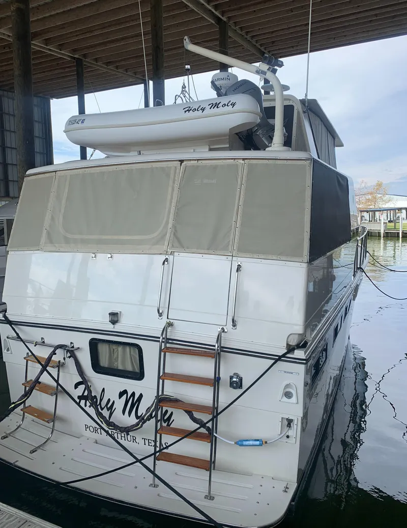 Slide: The Image of 1989 Carver Californian 48 yacht docked, featuring a covered deck and mounted dinghy. - 16